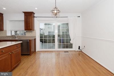kitchen featuring hanging light fixtures, light countertops, crown molding, light wood-type flooring, and dishwasher