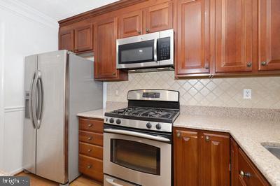kitchen featuring brown cabinetry, stainless steel appliances, decorative backsplash, and ornamental molding