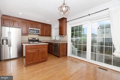kitchen with light wood-style flooring, stainless steel appliances, pendant lighting, a center island, and light countertops