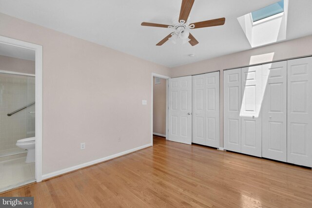 unfurnished bedroom with wood finished floors, ensuite bathroom, two closets, and a skylight