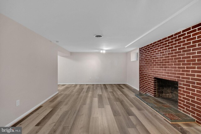 unfurnished living room featuring visible vents, baseboards, a brick fireplace, and wood finished floors