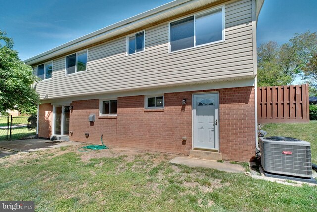 back of property with a lawn, brick siding, central AC, and fence