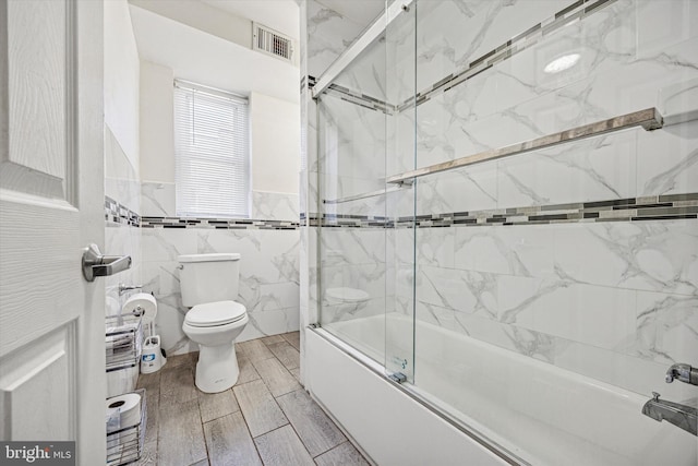 bathroom featuring wainscoting, toilet, enclosed tub / shower combo, tile walls, and visible vents