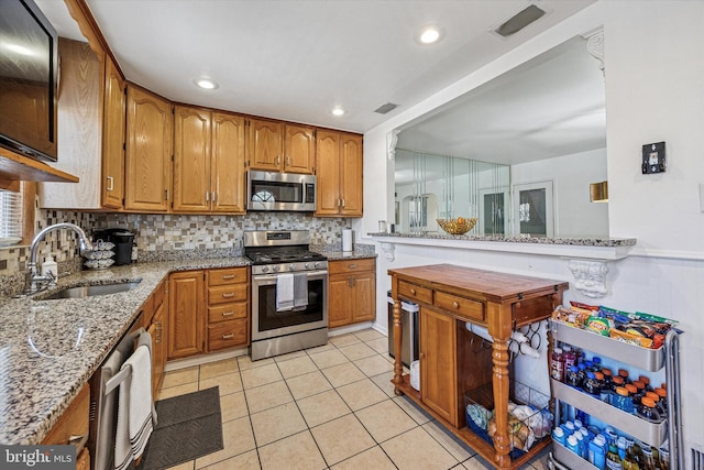kitchen with brown cabinetry, appliances with stainless steel finishes, tasteful backsplash, a sink, and light stone counters