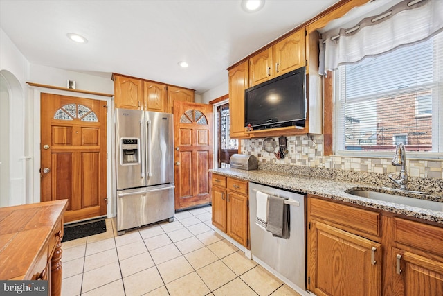 kitchen featuring stainless steel appliances, light stone countertops, plenty of natural light, and a sink