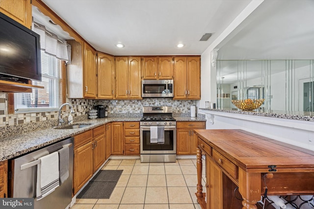 kitchen featuring backsplash, appliances with stainless steel finishes, a sink, light tile patterned floors, and light stone counters