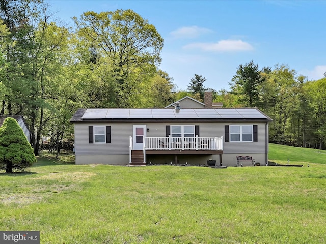 back of house with a lawn, a chimney, a deck, and solar panels