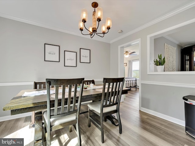 dining space with baseboards, ornamental molding, wood finished floors, and a notable chandelier