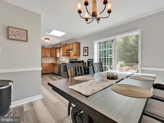 dining area with a skylight, ornamental molding, light wood-style flooring, and a chandelier