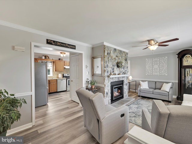 living room with a ceiling fan, a stone fireplace, ornamental molding, and light wood-style floors