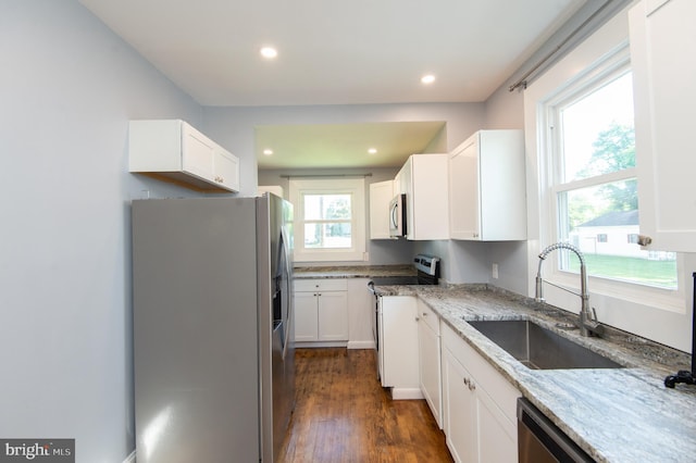 kitchen featuring stainless steel appliances, a sink, light stone counters, white cabinets, and recessed lighting