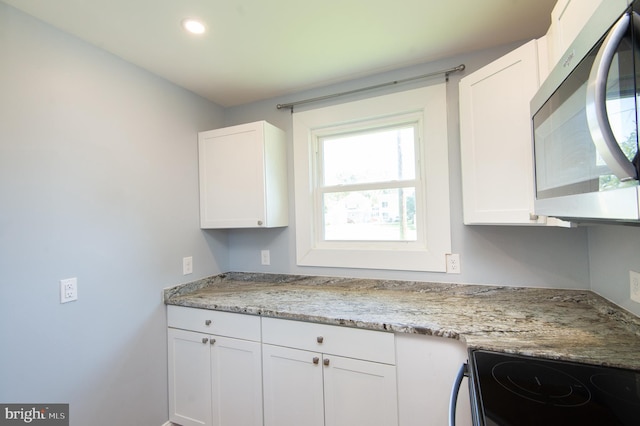 kitchen with stainless steel microwave, electric range, white cabinetry, light stone counters, and recessed lighting