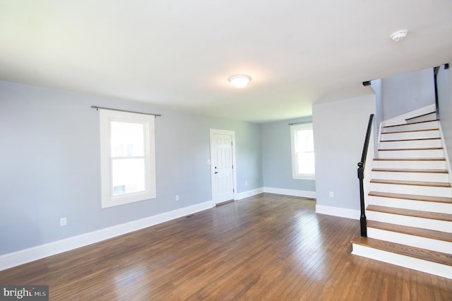unfurnished living room with baseboards, dark wood-type flooring, and stairway