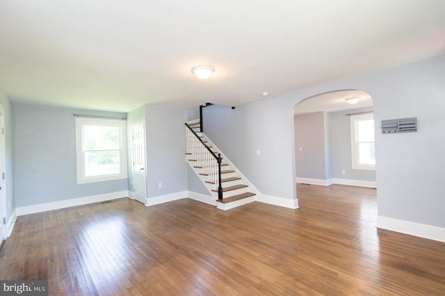 unfurnished living room featuring arched walkways, wood finished floors, stairway, and baseboards