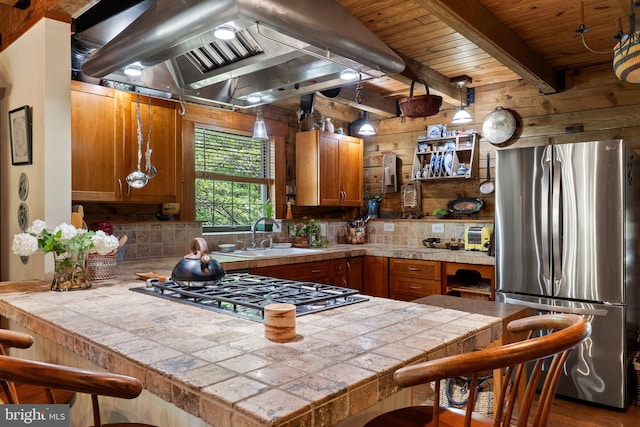 kitchen with brown cabinetry, light countertops, ventilation hood, a sink, and stainless steel appliances