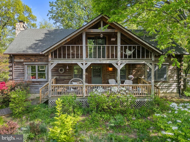 rear view of house with a deck, log exterior, a shingled roof, and a chimney