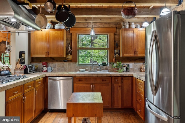 kitchen featuring brown cabinetry, under cabinet range hood, a sink, light wood finished floors, and appliances with stainless steel finishes