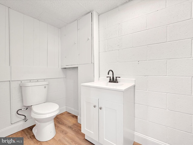 bathroom with a paneled ceiling, wood finished floors, concrete block wall, vanity, and toilet