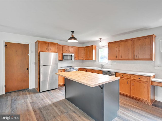 kitchen featuring a kitchen island, appliances with stainless steel finishes, a sink, light wood finished floors, and wood counters