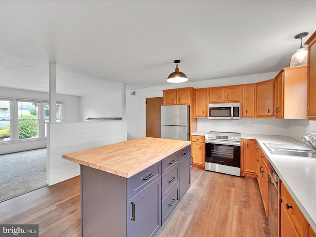 kitchen with appliances with stainless steel finishes, a sink, gray cabinetry, light wood-style floors, and wood counters