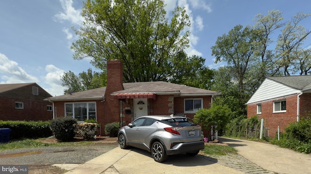 ranch-style house with brick siding, roof with shingles, a chimney, and concrete driveway
