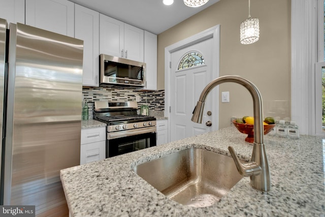 kitchen featuring backsplash, appliances with stainless steel finishes, a sink, light stone counters, and white cabinets