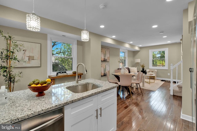 kitchen featuring light stone counters, a sink, white cabinetry, decorative light fixtures, and hardwood / wood-style flooring