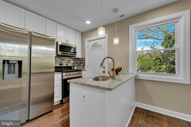 kitchen featuring a peninsula, baseboards, light stone counters, a sink, and stainless steel appliances
