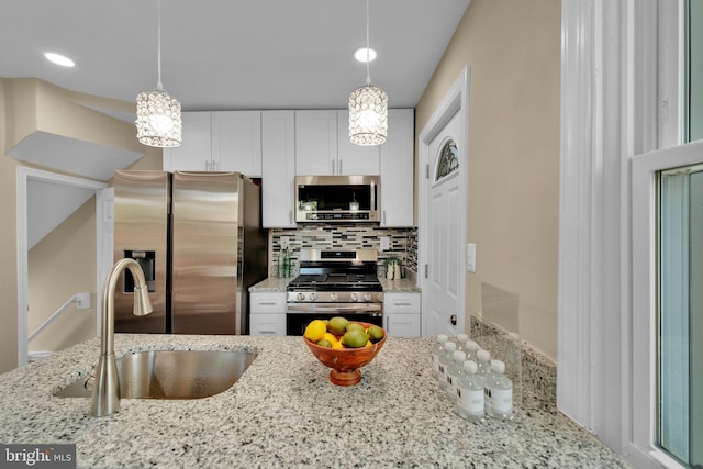 kitchen with decorative backsplash, light stone countertops, white cabinets, a sink, and stainless steel appliances