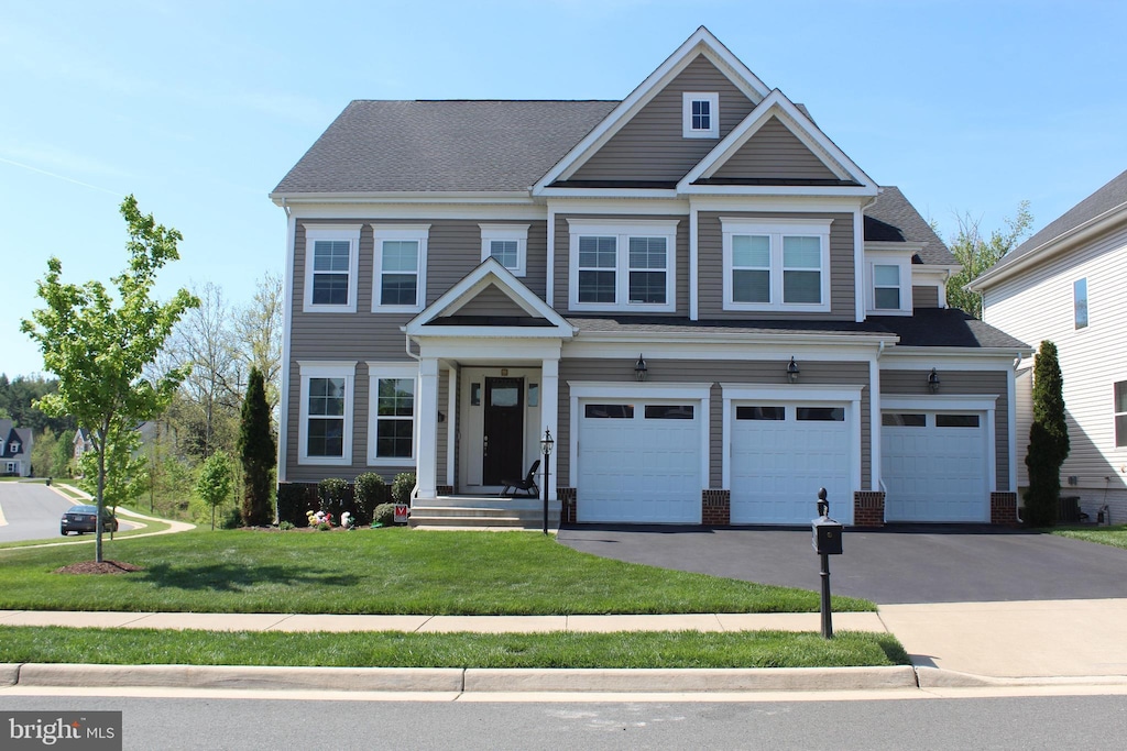 craftsman-style house with brick siding, an attached garage, a front lawn, and aphalt driveway