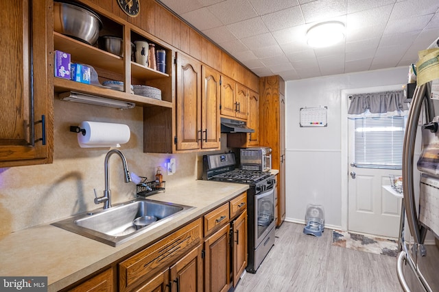 kitchen with brown cabinetry, a sink, under cabinet range hood, and stainless steel appliances