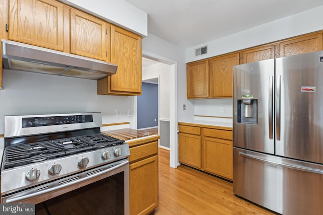 kitchen with appliances with stainless steel finishes, light wood-style floors, light countertops, under cabinet range hood, and visible vents