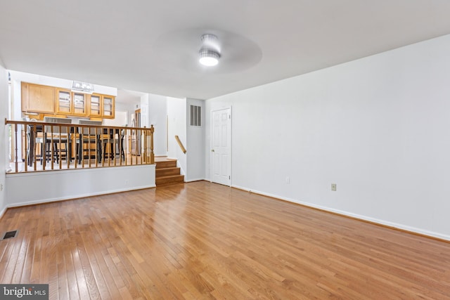 unfurnished living room featuring visible vents, light wood-style floors, baseboards, ceiling fan, and stairway