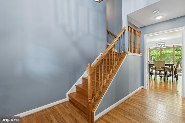 staircase with baseboards, an inviting chandelier, and hardwood / wood-style flooring