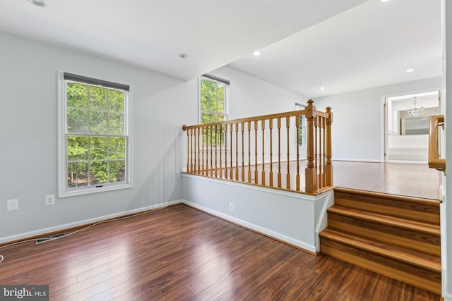 empty room featuring an inviting chandelier, visible vents, stairs, wood finished floors, and baseboards
