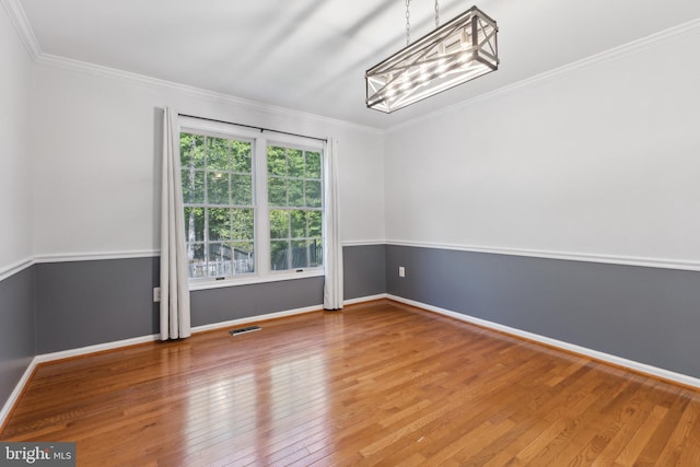 spare room featuring baseboards, ornamental molding, wood finished floors, and visible vents