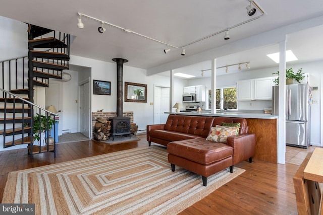 living area featuring stairway, track lighting, wood-type flooring, and a wood stove