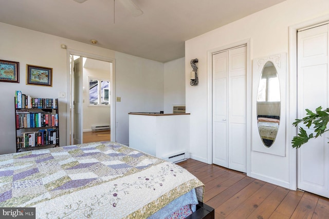 bedroom with wood-type flooring, multiple closets, and a baseboard heating unit