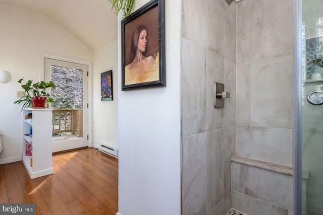 full bath featuring wood finished floors, baseboard heating, vaulted ceiling, and tiled shower
