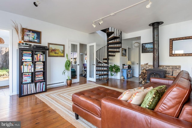 living area with track lighting, a wood stove, stairs, wood finished floors, and baseboard heating