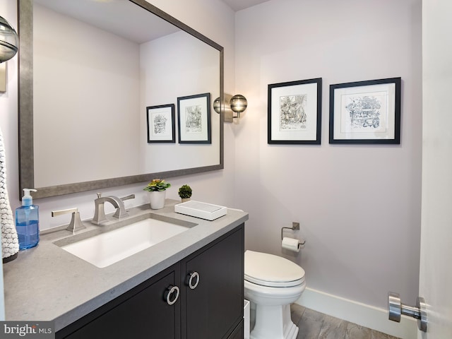 half bath featuring vanity, baseboards, and toilet