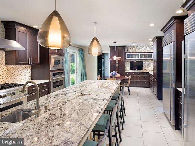 kitchen with a sink, pendant lighting, built in appliances, and backsplash
