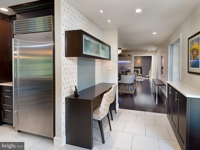 kitchen with dark brown cabinets, light tile patterned floors, built in fridge, glass insert cabinets, and recessed lighting