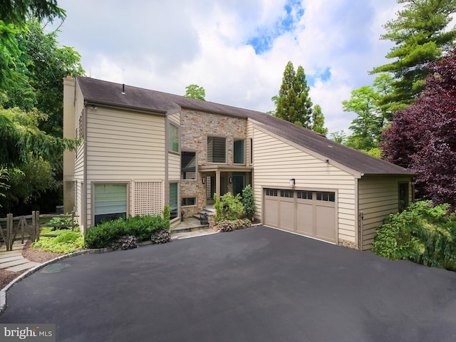 view of front of house featuring a chimney, an attached garage, driveway, and stone siding