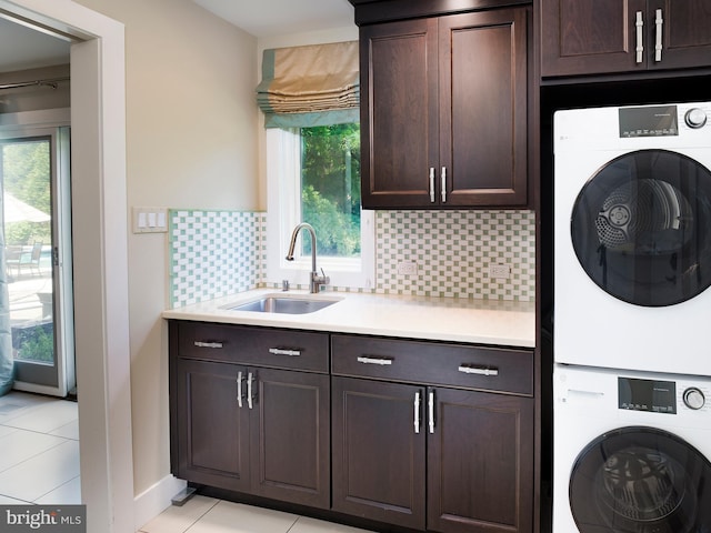 laundry room featuring a sink, stacked washer and dryer, cabinet space, and light tile patterned floors