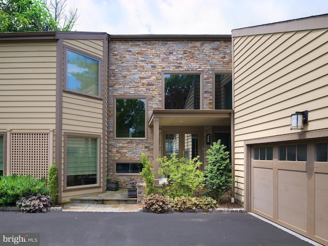 view of front of property featuring an attached garage, stone siding, and aphalt driveway