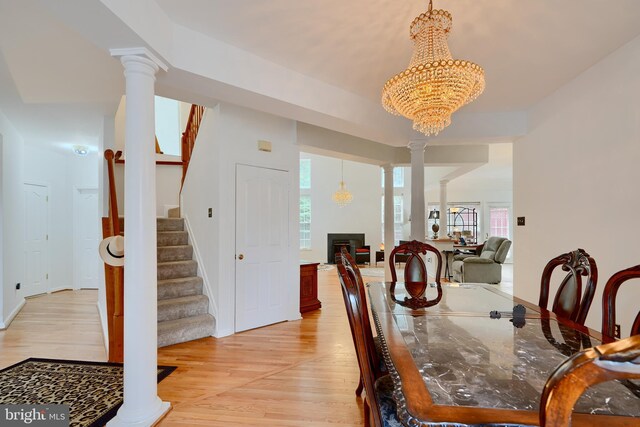 dining room featuring stairs, light wood-type flooring, decorative columns, and a chandelier