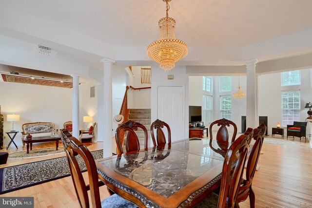 dining room with healthy amount of natural light, light wood finished floors, stairway, and ornate columns