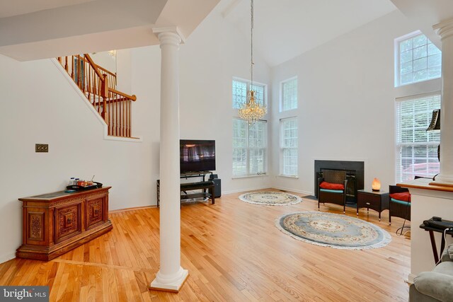 living room featuring a towering ceiling, decorative columns, healthy amount of natural light, and wood finished floors