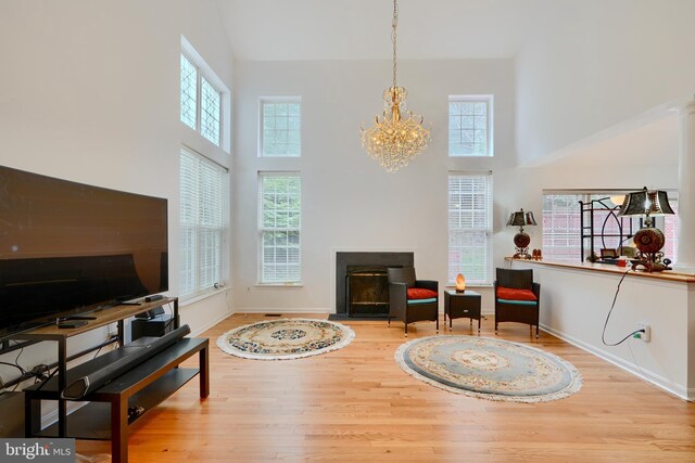 sitting room featuring a towering ceiling, wood finished floors, a chandelier, a fireplace with flush hearth, and baseboards